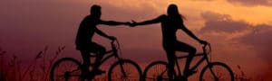 two people riding on a bike in the sunset holding hands